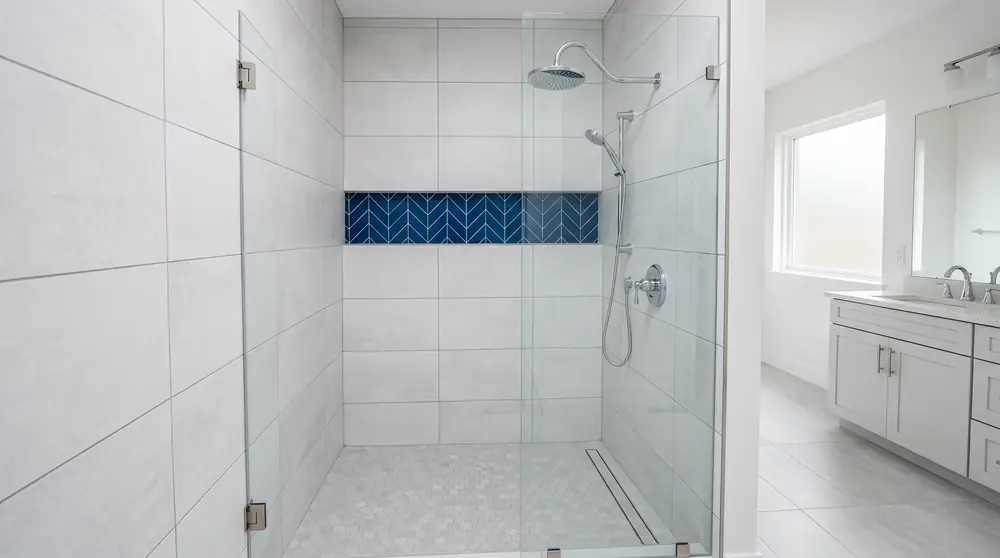 Regadera moderna reci&eacute;n remodelada con azulejo blanco, cristal y una franja azul marino